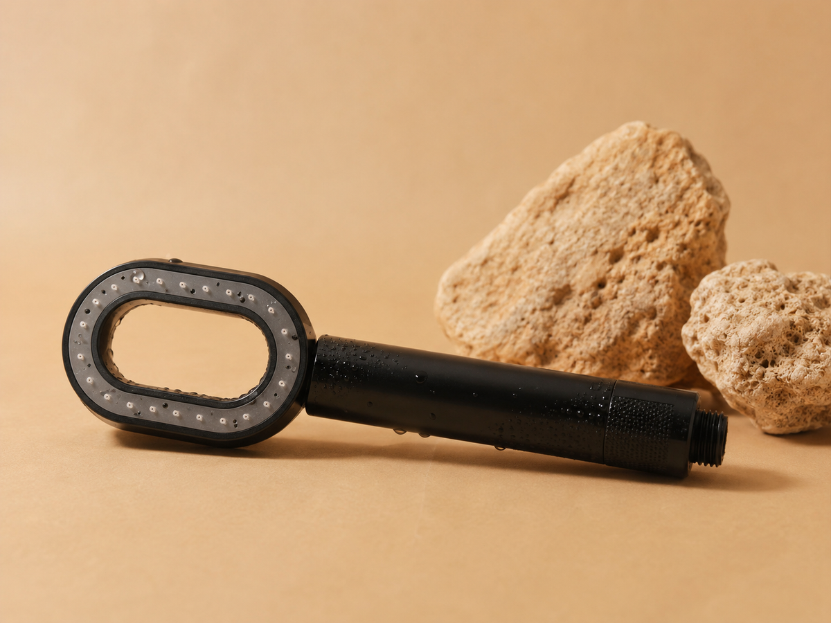 Pommeau de douche filtrant ZEWANI noir posé sur des pierres, fond beige
