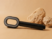 Pommeau de douche filtrant ZEWANI noir posé sur des pierres, fond beige